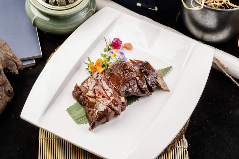 白瓷盘装的苏州酱鸭摆放在寿司帘上图片