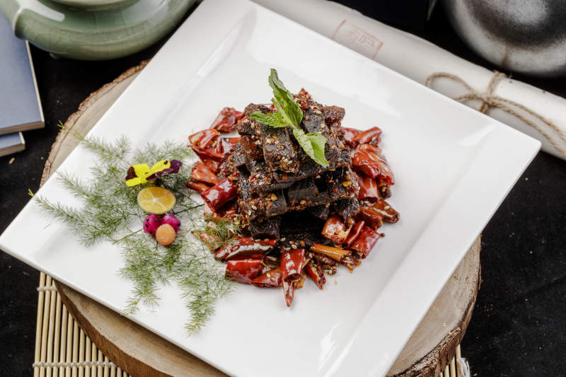 方形瓷盘装的麻辣牛肉摆放在樟木砧板上图片