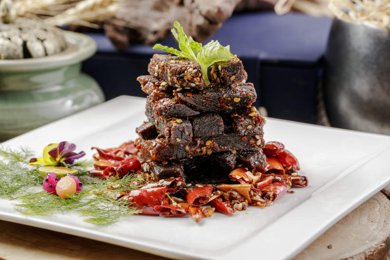 方形瓷盘装的麻辣牛肉摆放在樟木砧板上图片