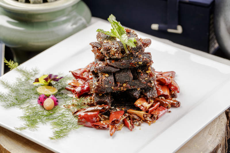 方形瓷盘装的麻辣牛肉摆放在樟木砧板上图片