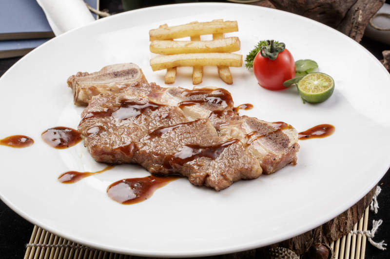 圆形白瓷盘装的香煎牛仔骨摆放在寿司帘上图片