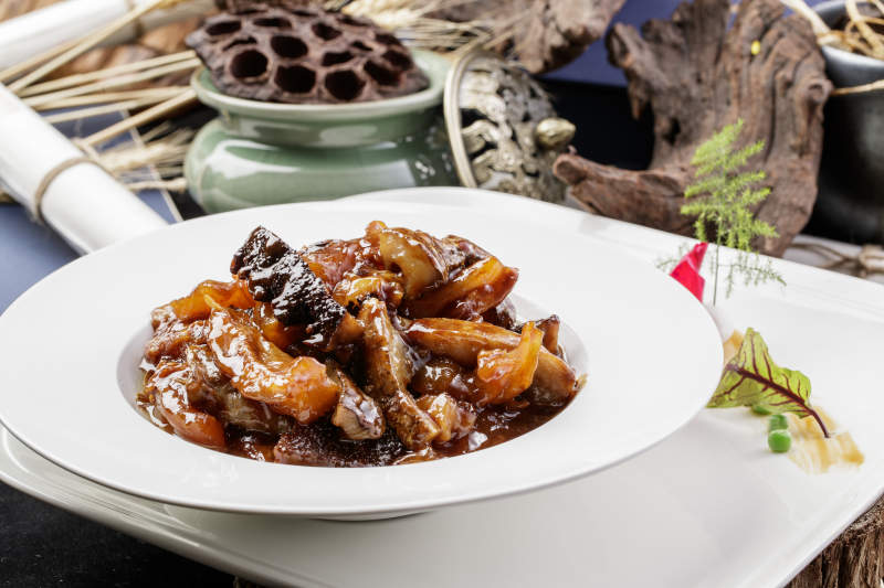 圆形白瓷盘装的葱烧梅花参摆放在黑色背景上图片