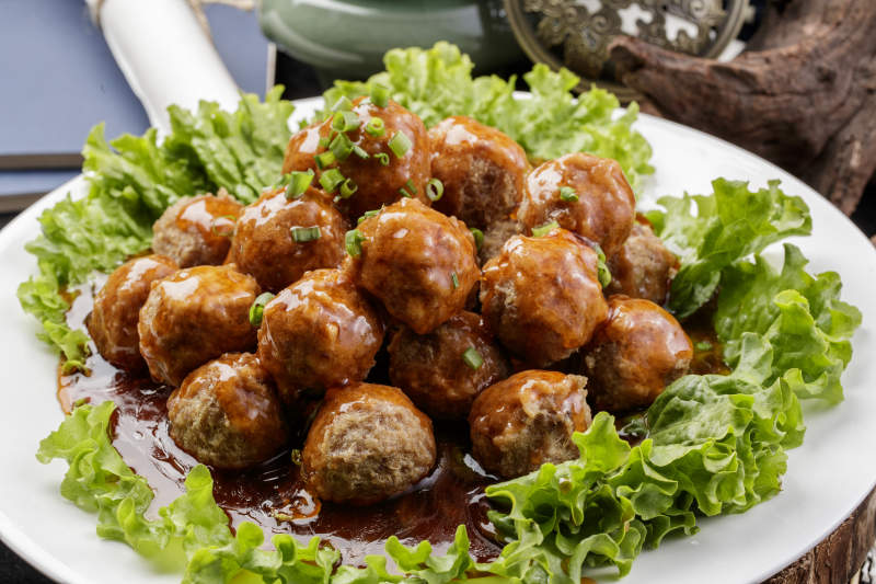 白色圆瓷盘装的红烧丸子摆放在樟木砧板上图片