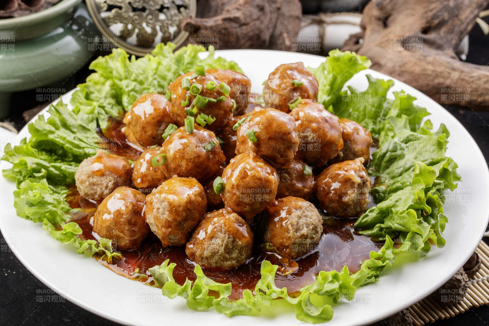 白色圆瓷盘装的红烧丸子摆放在樟木砧板上图片