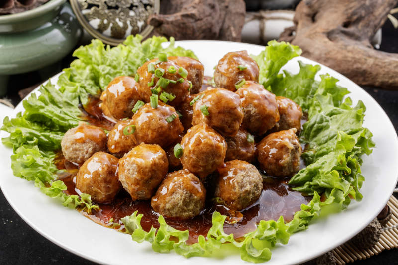 白色圆瓷盘装的红烧丸子摆放在樟木砧板上图片