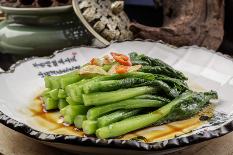 白色瓷盘装的炝炒芥蓝摆放在樟木砧板上图片