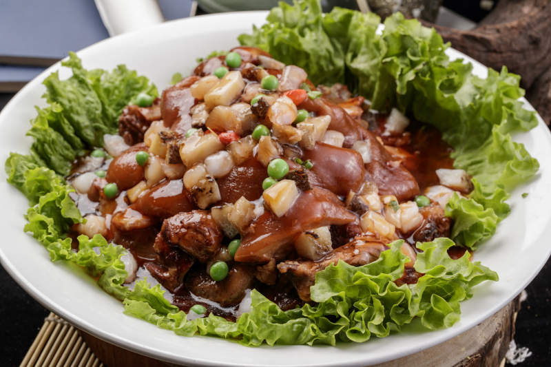 圆形瓷盘装的红扒大肘子摆放在樟木砧板上图片