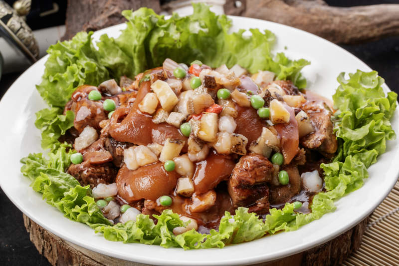 圆形瓷盘装的红扒大肘子摆放在樟木砧板上图片