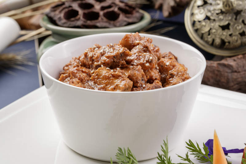 白色瓷碗装的黑胡椒猪小排摆放在黑色背景上图片