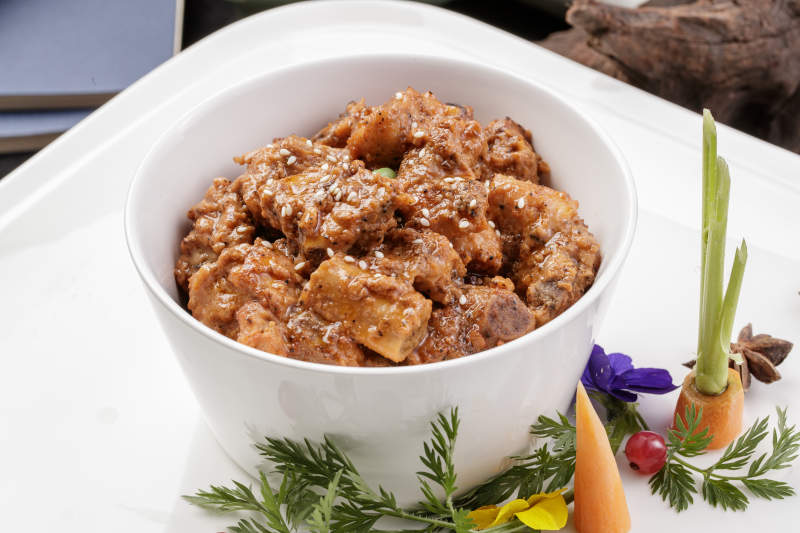 白色瓷碗装的黑胡椒猪小排摆放在黑色背景上图片