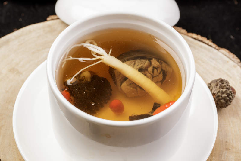 白色汤盅装的羊肚菌人参汤摆放在樟木砧板上图片