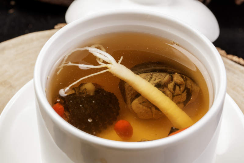 白色汤盅装的羊肚菌人参汤摆放在樟木砧板上图片