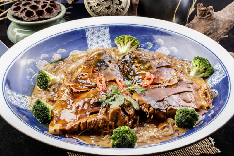 青花瓷盘装的垮炖大鱼头摆放在寿司帘上图片
