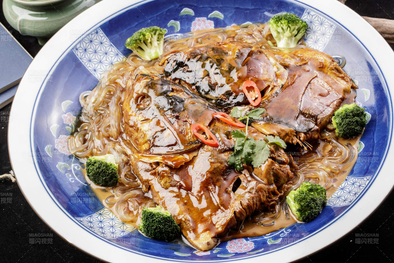 青花瓷盘装的垮炖大鱼头摆放在寿司帘上图片