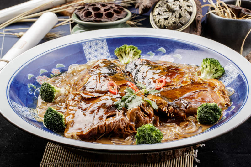 青花瓷盘装的垮炖大鱼头摆放在寿司帘上图片