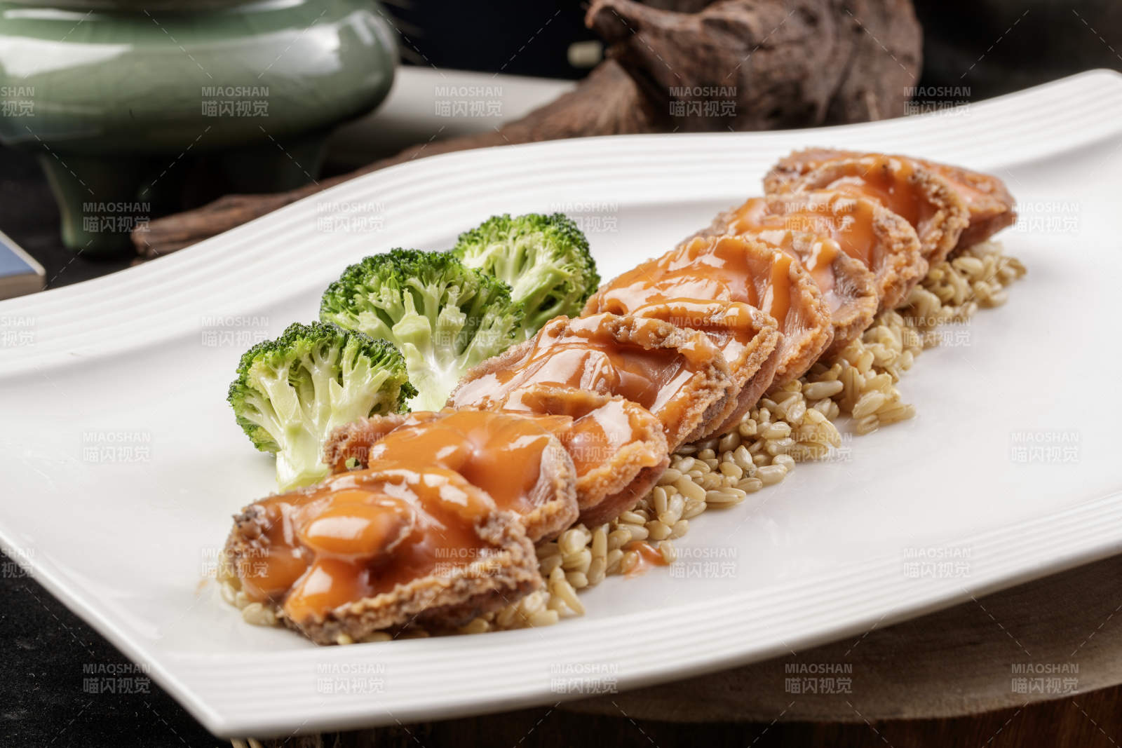 长方形瓷盘装的浓汁薏米鲜鲍鱼摆放在樟木砧板上图片