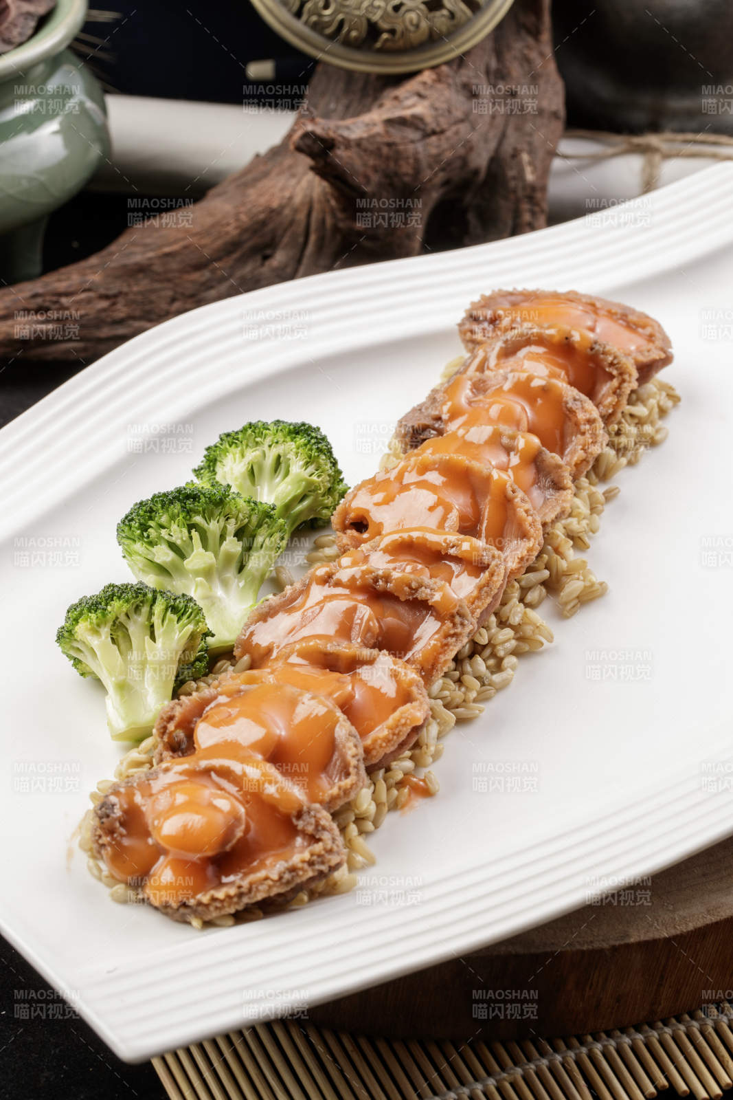 长方形瓷盘装的浓汁薏米鲜鲍鱼摆放在樟木砧板上图片