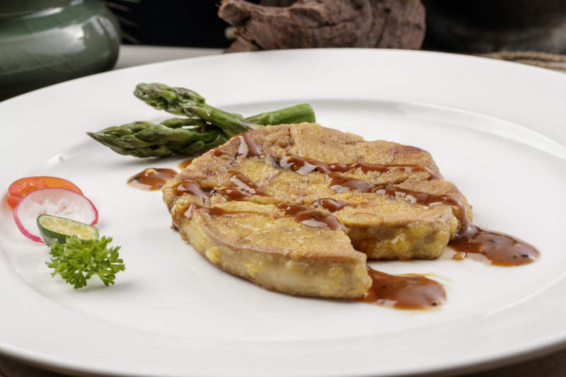 白色圆形瓷盘装的香煎法式鹅肝摆放在樟木砧板上图片