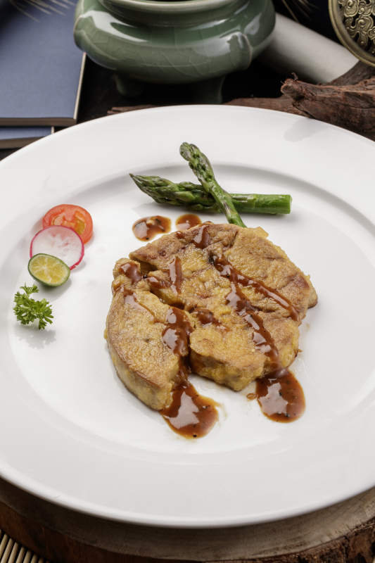 白色圆形瓷盘装的香煎法式鹅肝摆放在樟木砧板上图片