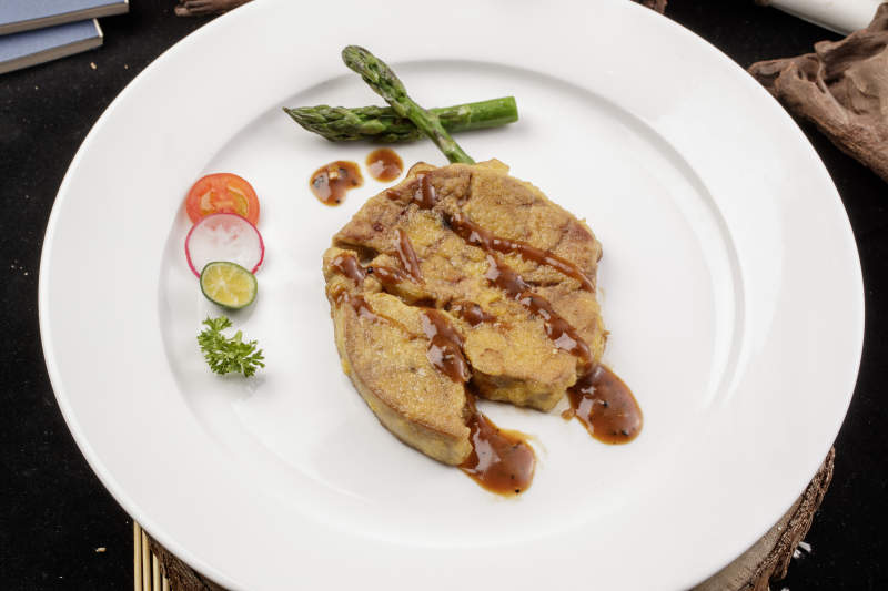 白色圆形瓷盘装的香煎法式鹅肝摆放在樟木砧板上图片