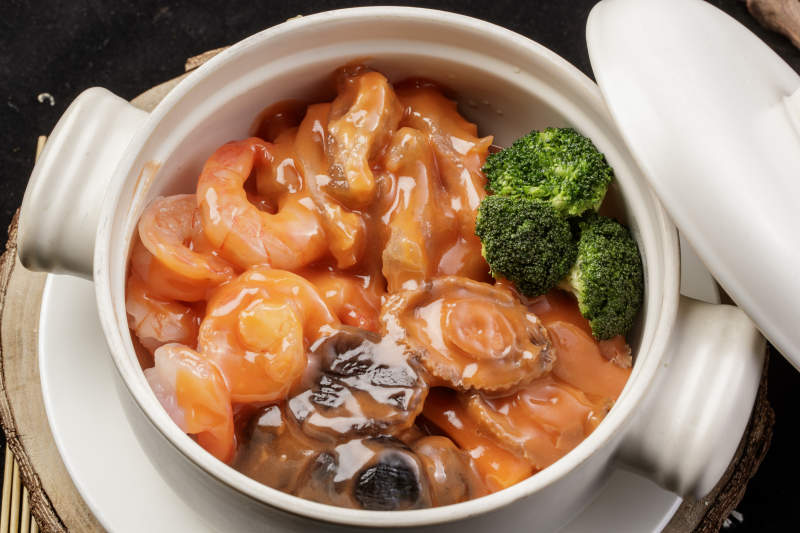 白色瓷砂锅装的浓汤海鲜煲摆放在寿司帘图片