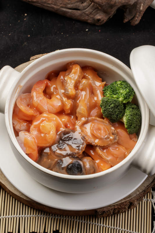 白色瓷砂锅装的浓汤海鲜煲摆放在寿司帘图片