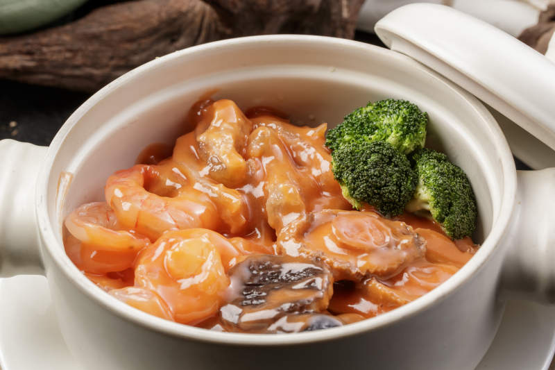 白色瓷砂锅装的浓汤海鲜煲摆放在寿司帘图片