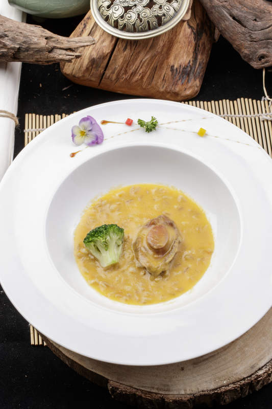 圆形白瓷盘装的薏米鲍鱼羹摆放在樟木砧板上图片