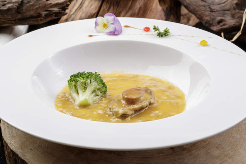 圆形白瓷盘装的薏米鲍鱼羹摆放在樟木砧板上图片