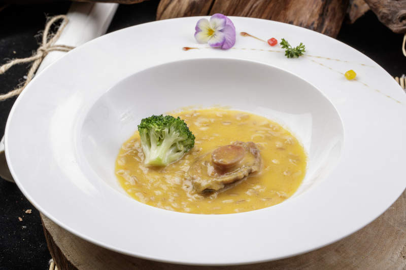 圆形白瓷盘装的薏米鲍鱼羹摆放在樟木砧板上图片