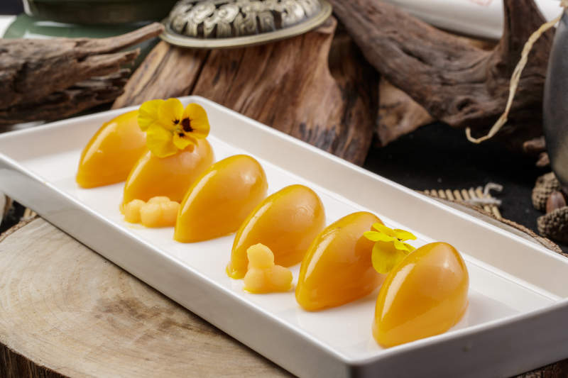 长方形瓷盘装的芒果冻摆放在樟木砧板上图片