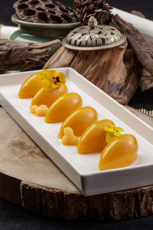 长方形瓷盘装的芒果冻摆放在樟木砧板上图片
