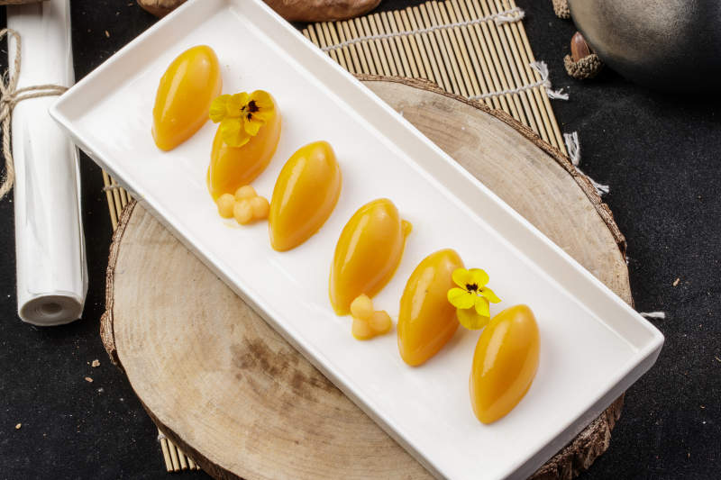 长方形瓷盘装的芒果冻摆放在樟木砧板上图片