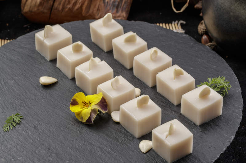 圆形黑色石盘装的奶香杏仁糕摆放在寿司帘上图片