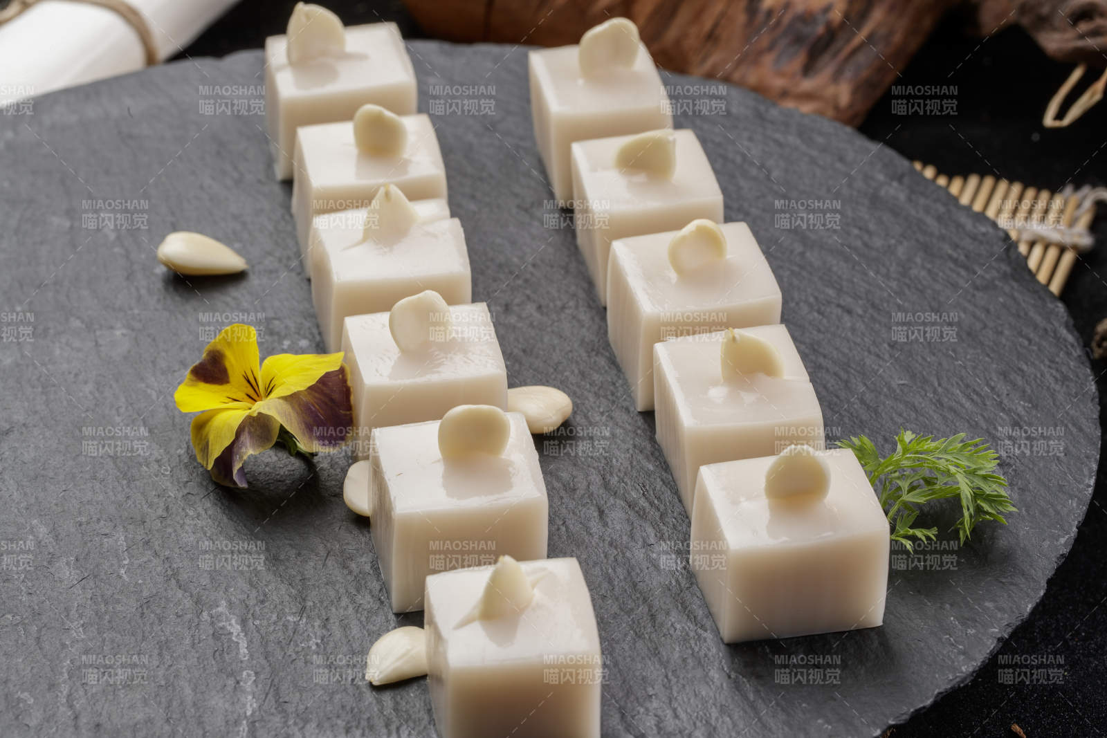 圆形黑色石盘装的奶香杏仁糕摆放在寿司帘上图片