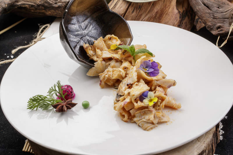 圆形瓷盘装的温拌海螺片摆放在寿司帘上图片