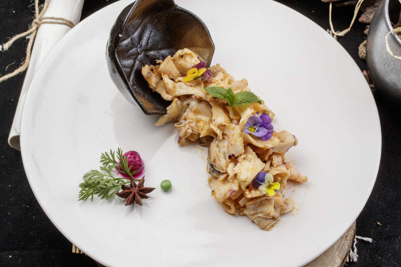 圆形瓷盘装的温拌海螺片摆放在寿司帘上图片