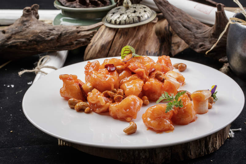 白色圆盘装的宫保大虾球摆放在寿司帘上图片