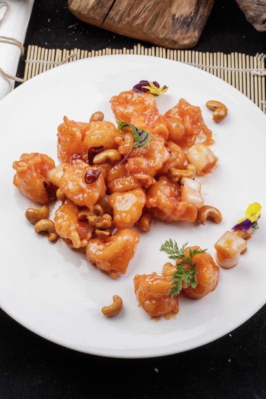 白色圆盘装的宫保大虾球摆放在寿司帘上图片