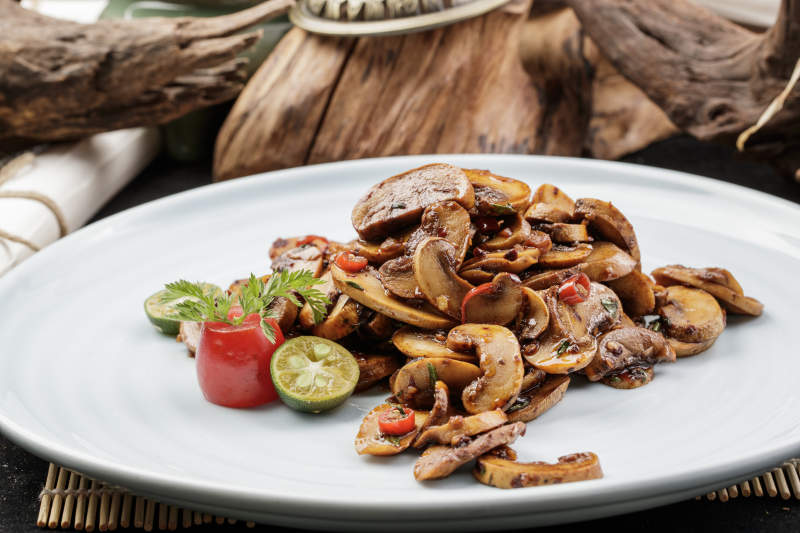 青瓷盘装的川味酱爆鲜口蘑摆放在寿司帘上图片