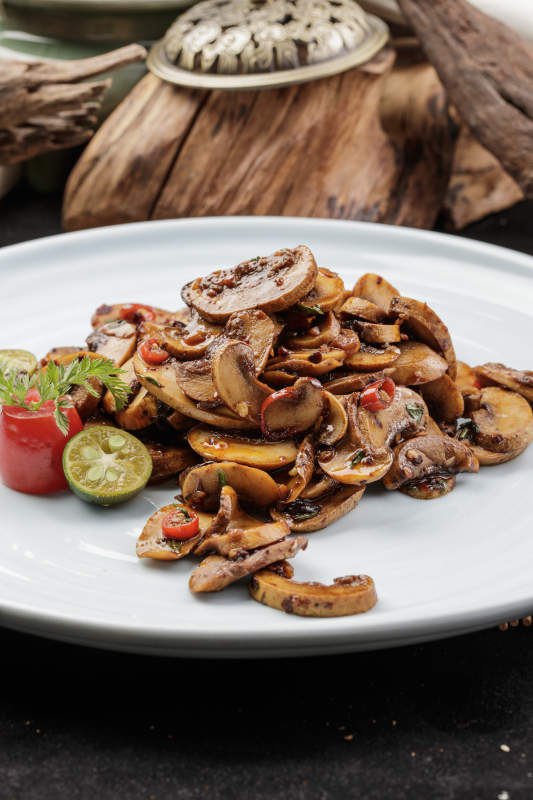 青瓷盘装的川味酱爆鲜口蘑摆放在寿司帘上图片