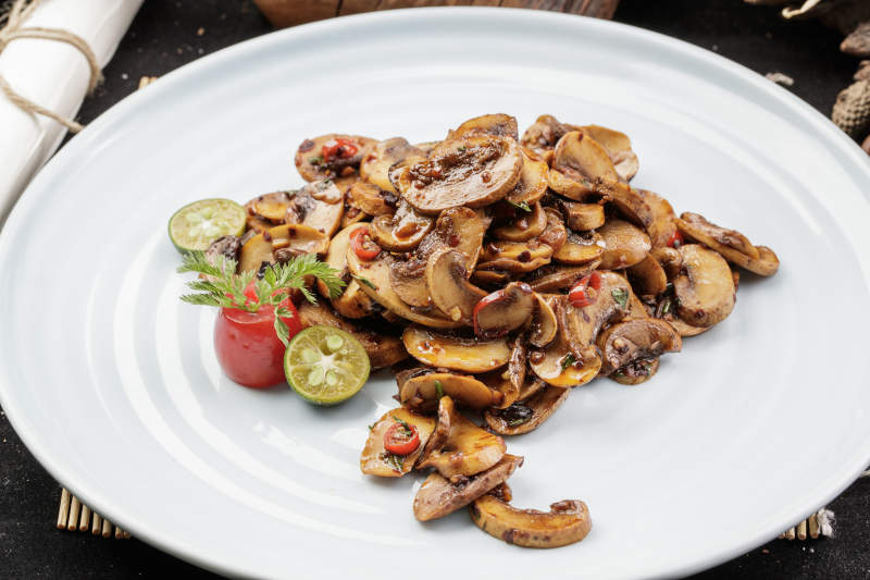 青瓷盘装的川味酱爆鲜口蘑摆放在寿司帘上图片