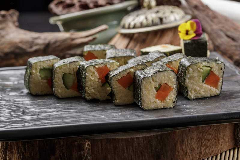 黑色石盘装的小米寿司卷摆放在樟木砧板上图片