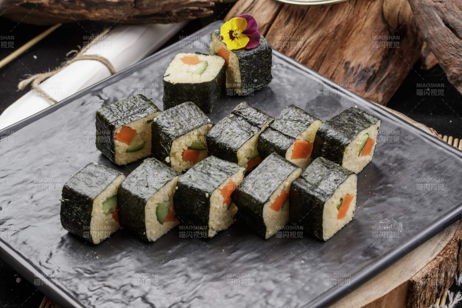 黑色石盘装的小米寿司卷摆放在樟木砧板上图片