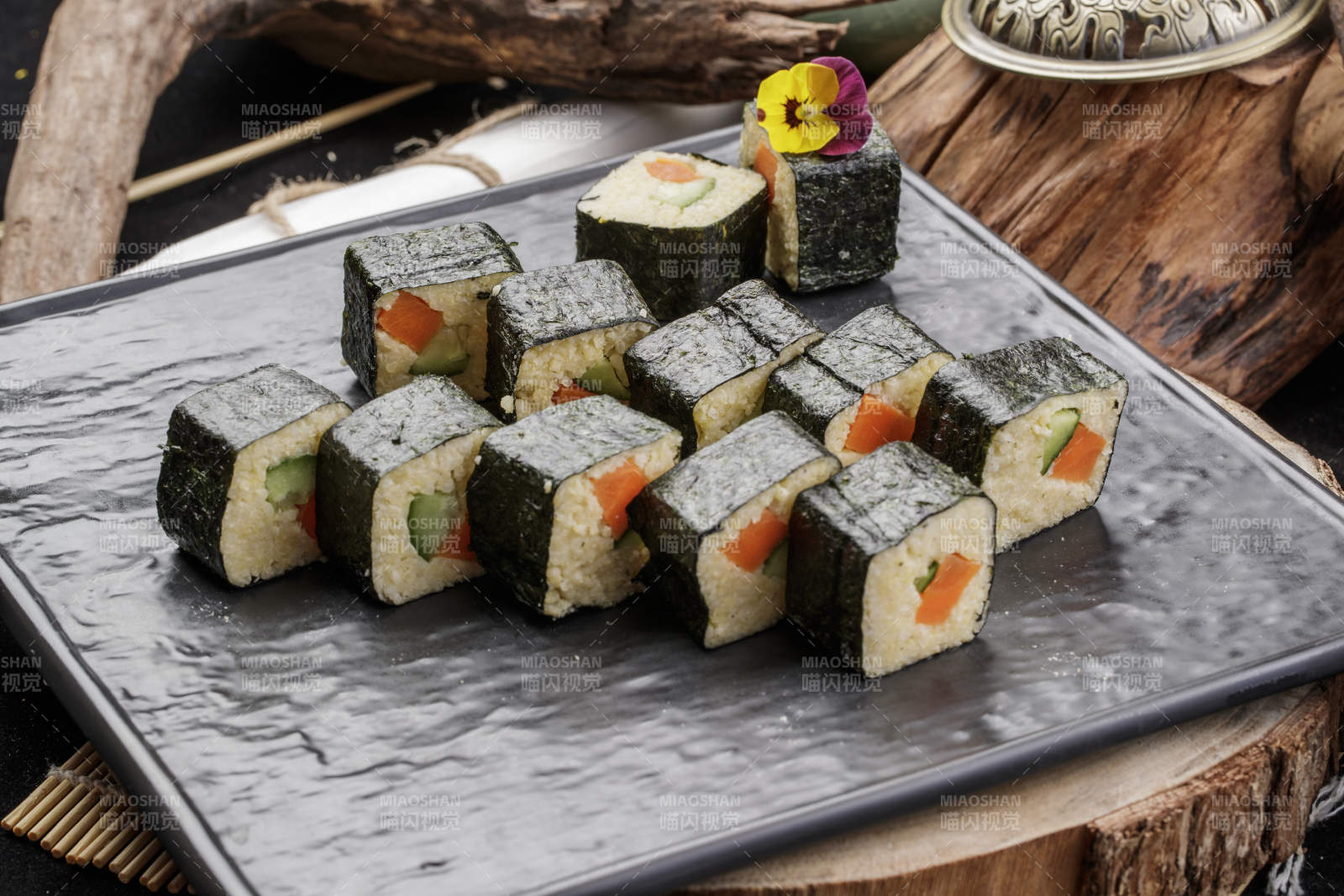 黑色石盘装的小米寿司卷摆放在樟木砧板上图片