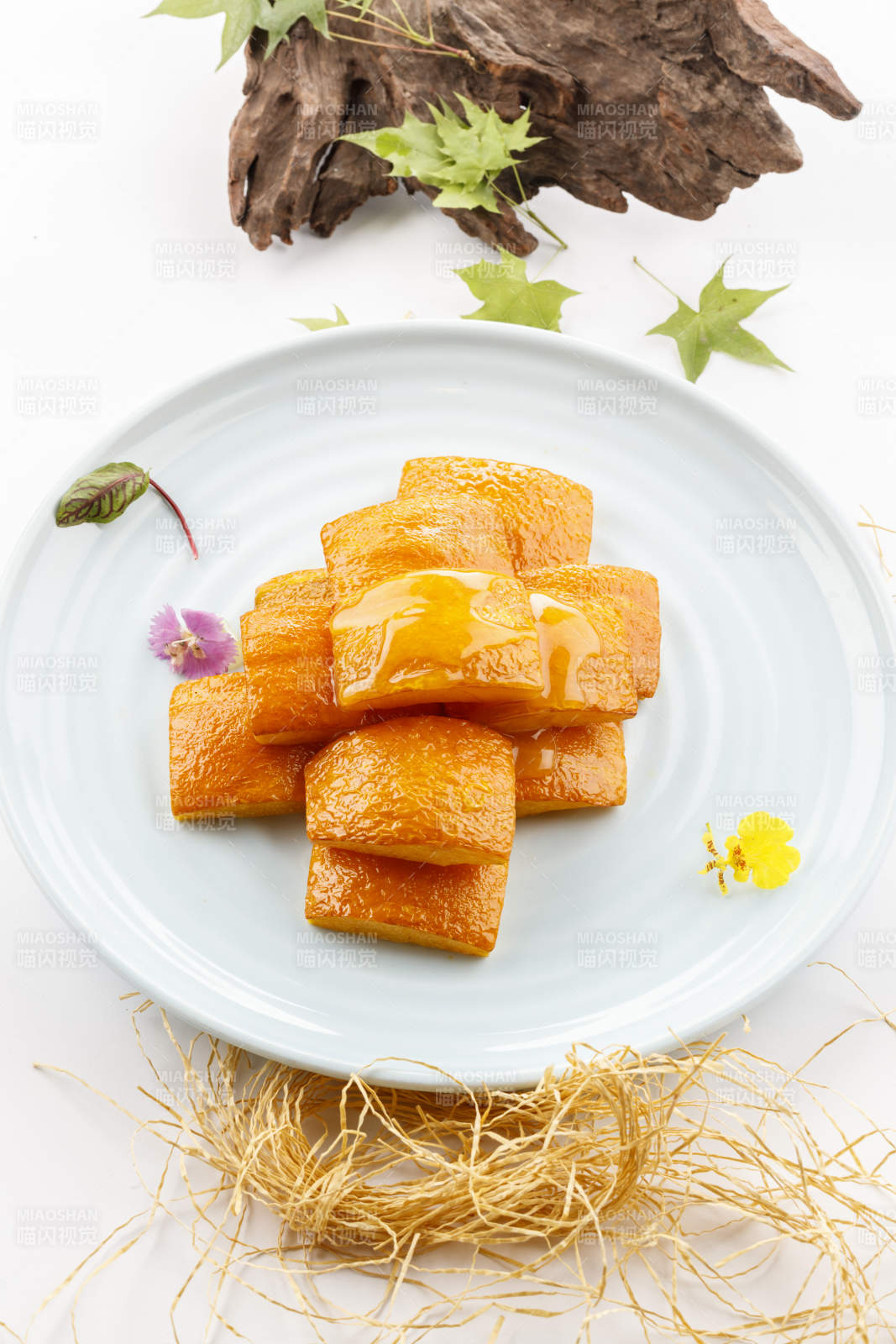 青瓷盘装的蜂蜜焗南瓜摆放在白色背景上图片