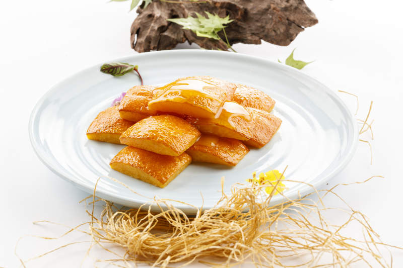 青瓷盘装的蜂蜜焗南瓜摆放在白色背景上图片