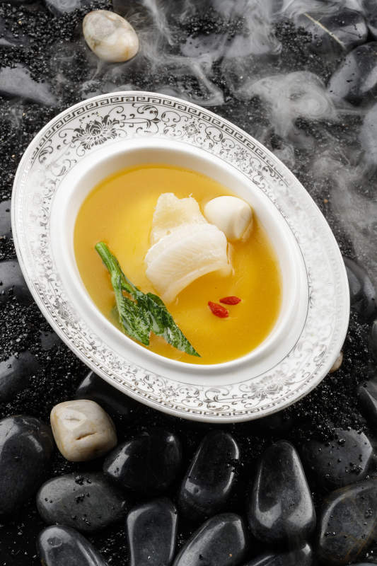 浓汤鱼唇摆放在干冰缭绕的鹅卵石上图片