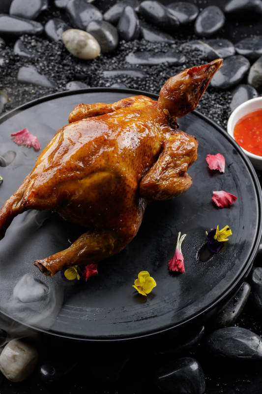 黑色底盘装的港式脆皮鸡摆放在黑色鹅卵石上图片