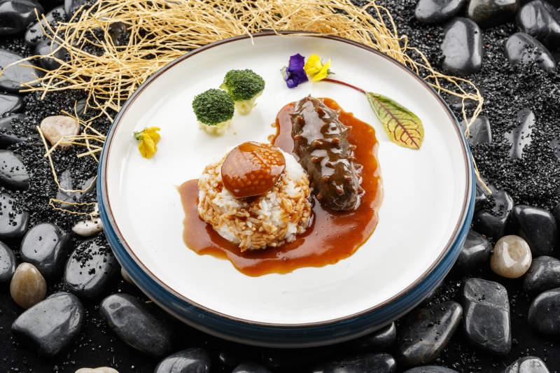 鲜鲍鱼辽参捞饭摆放在黑色鹅卵石上图片